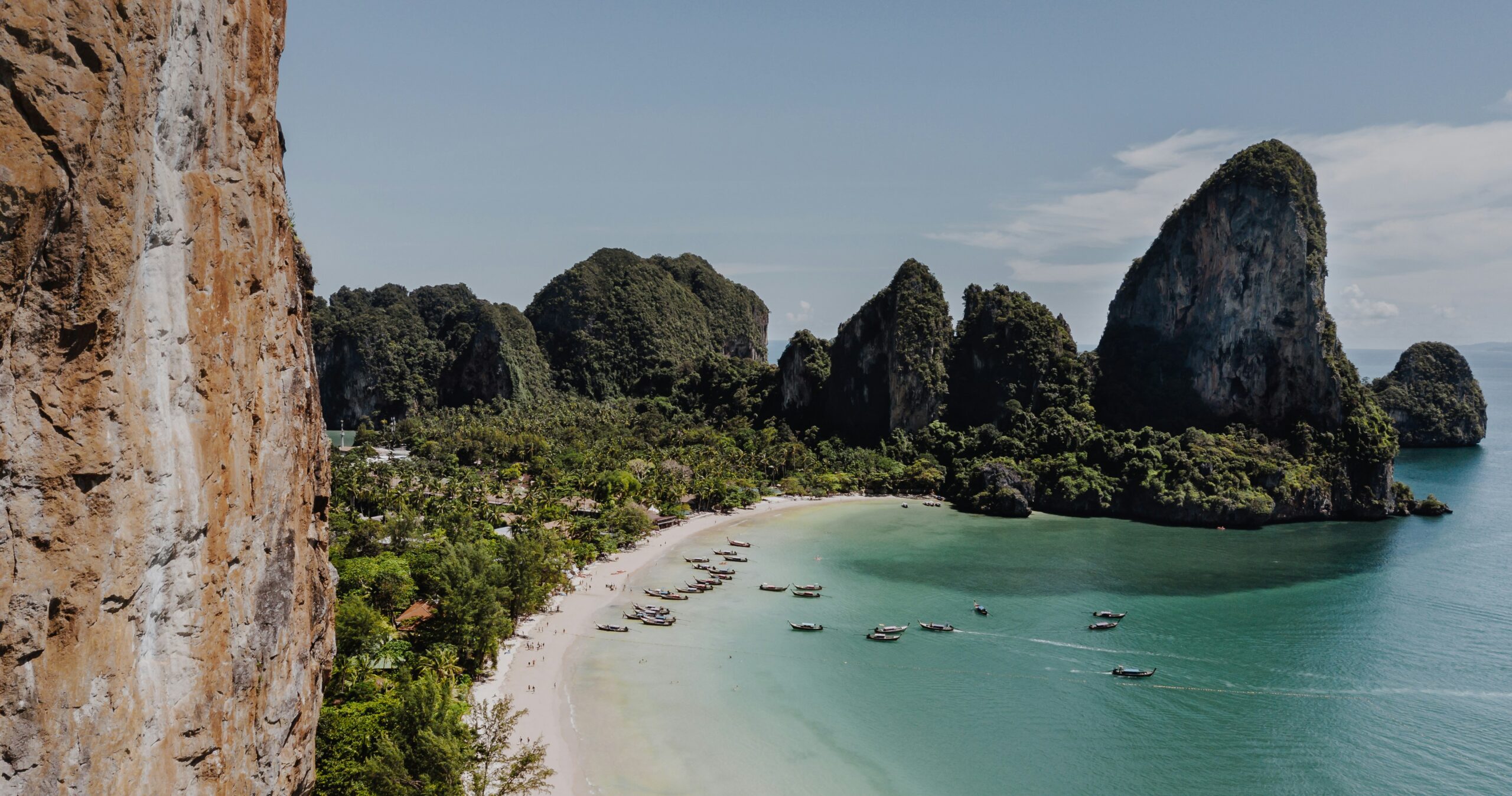 Plage tropicale de Krabi avec falaises spectaculaires, eau turquoise et bateaux traditionnels en Thaïlande