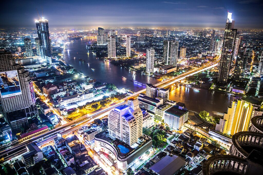 Vue panoramique de Bangkok de nuit avec les gratte-ciels illuminés et la rivière Chao Phraya — une atmosphère typique des rooftops de la capitale thaïlandaise.