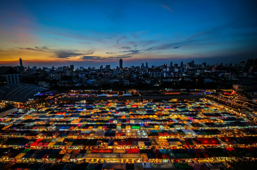 Vue nocturne spectaculaire d’un marché de Bangkok, avec des stands colorés et des lumières vives typiques des night markets thaïlandais.